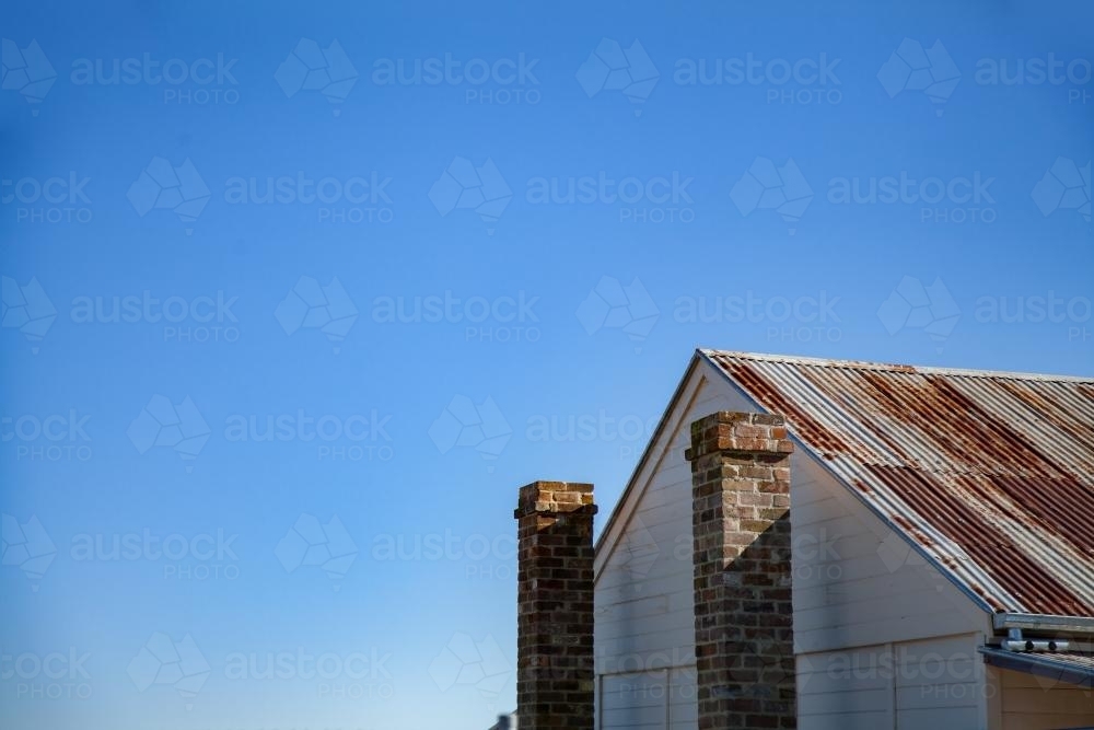 Rusty roof and stone chimney of old building against blue sky - Australian Stock Image