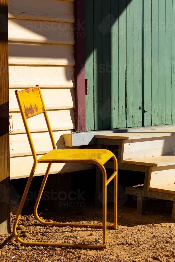 rusty yellow metal chair, green door and steps - Australian Stock Image
