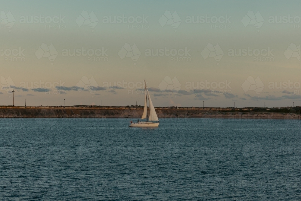 Sail boat entering the Hunter River past the Nobby's Beach breakwall at Newcastle, NSW - Australian Stock Image