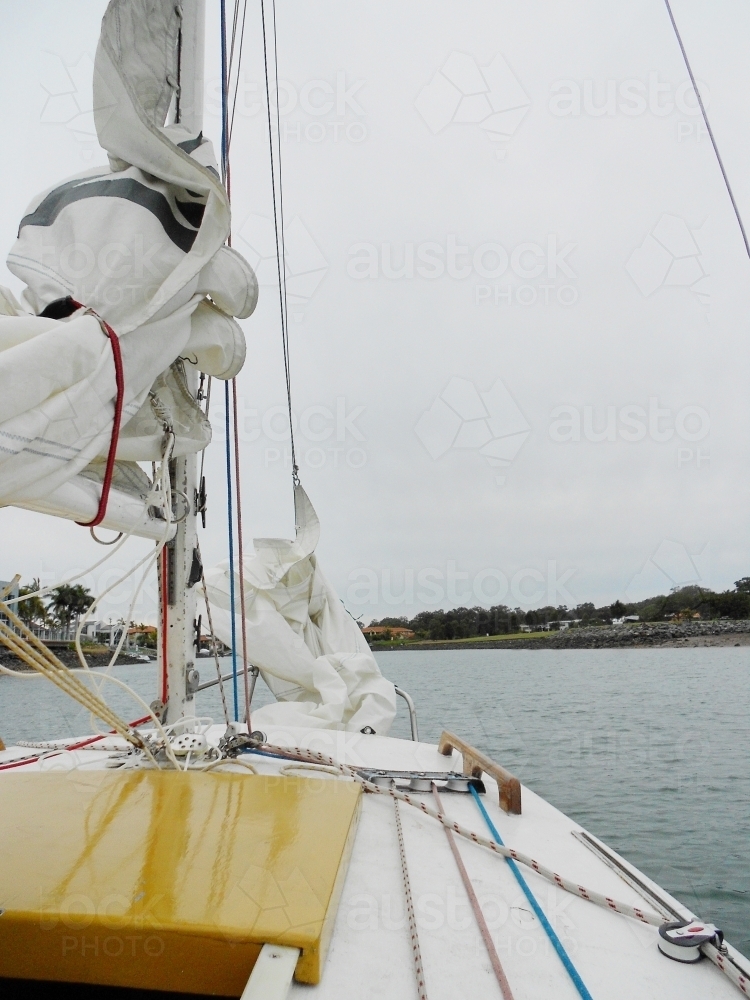 sailboat sailing out of harbour on overcast day - Australian Stock Image