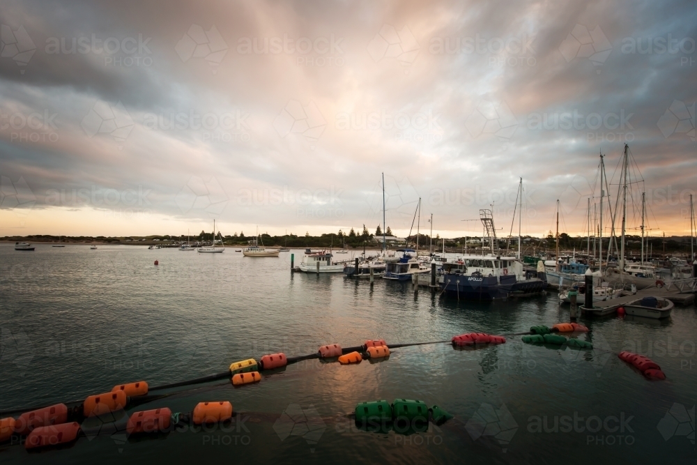 Sailing boats and fishing boats in a harbor at dusk - Australian Stock Image