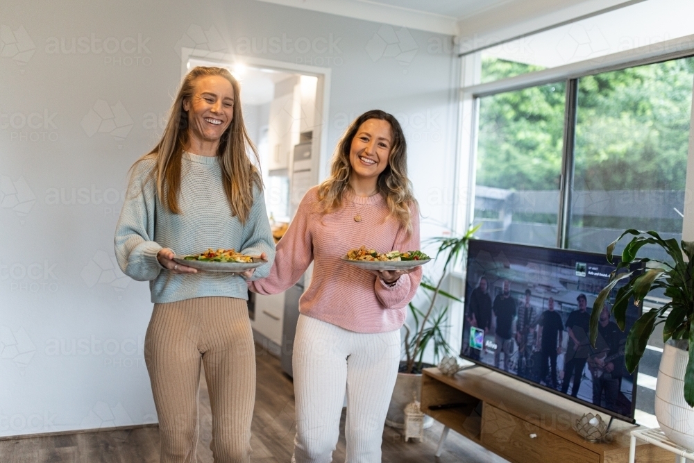 Same sex couple carrying their plates of food together at home - Australian Stock Image