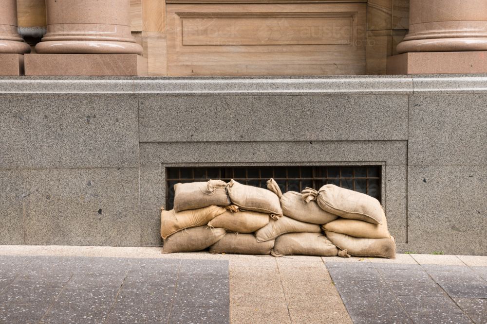 Sandbags along the footpath lining the lower windows of a building in Brisbane CBD before a cyclone - Australian Stock Image