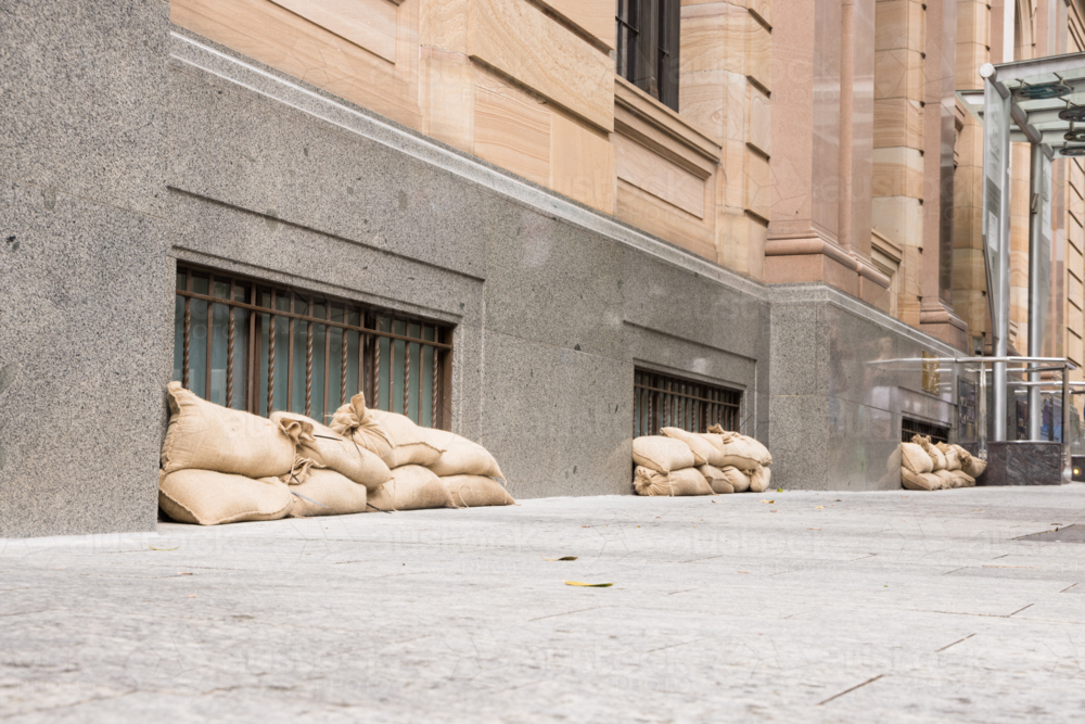 Sandbags along the footpath lining the lower windows of a building in Brisbane CBD before a cyclone - Australian Stock Image