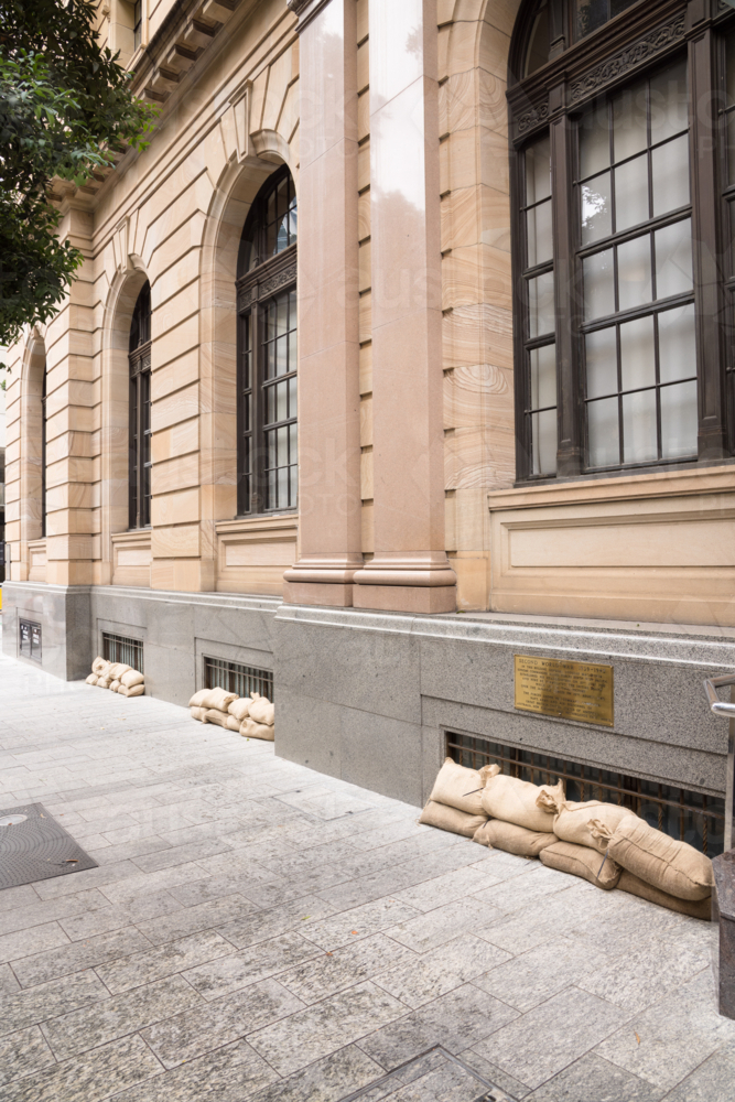 Sandbags along the footpath lining the lower windows of a building in Brisbane CBD before a cyclone - Australian Stock Image
