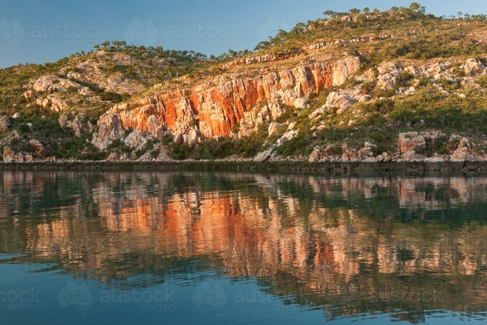 Sandstone cliffs reflected in calm water - Australian Stock Image