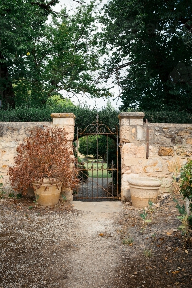 Sandstone wall with iron gate leading to green garden - Australian Stock Image