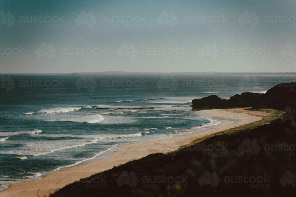 Sandy beach with gentle waves and rocky cliffs - Australian Stock Image