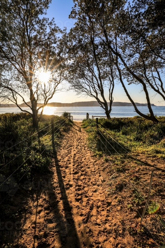 Sandy pathway leading to sun rising over ocean - Australian Stock Image