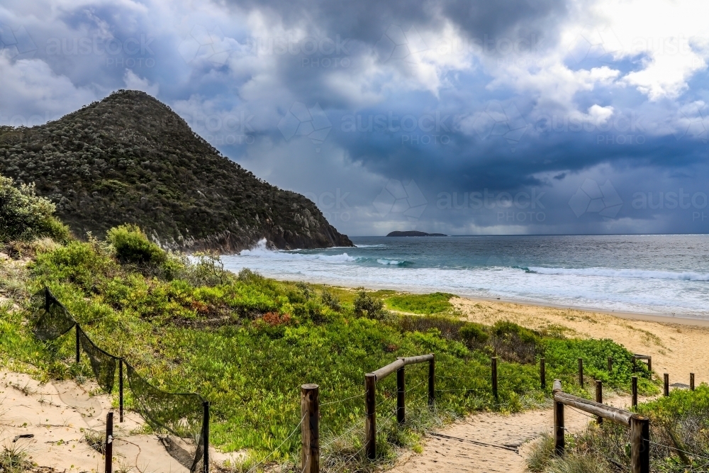 Sandy track leading to beach against mountain and cloudy sky - Australian Stock Image