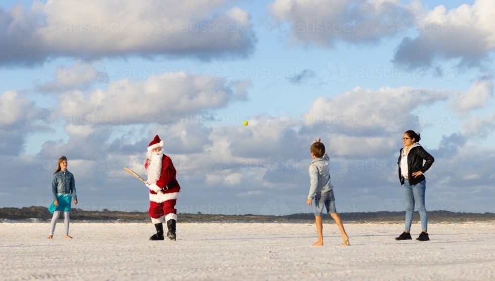 Santa and kids playing beach cricket in front of a cloudy sky - Australian Stock Image