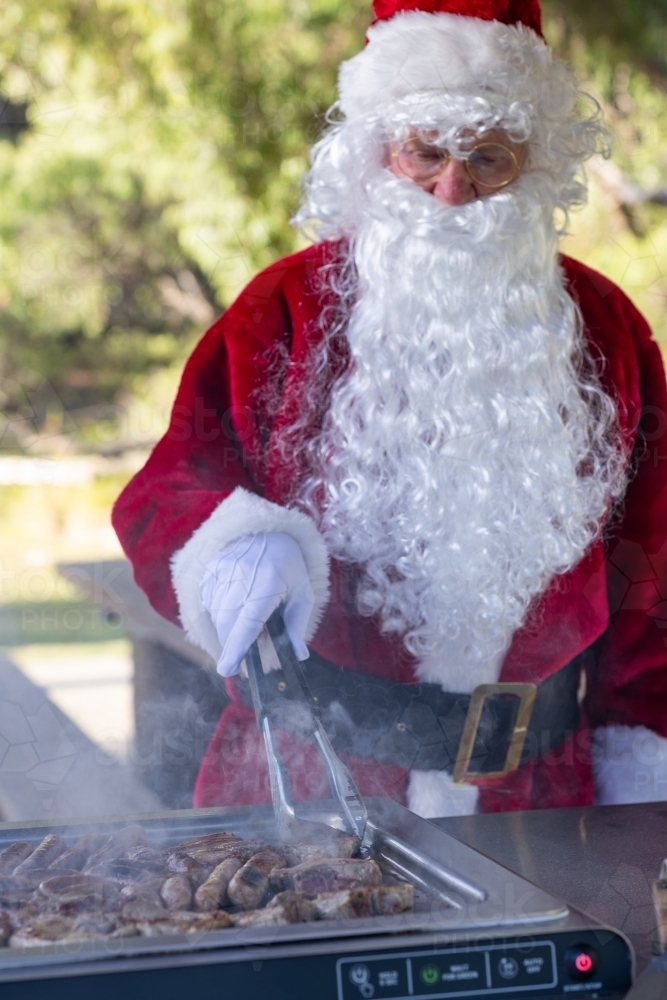 santa claus cooking lamb chops and sausages on a bbq in a park - Australian Stock Image