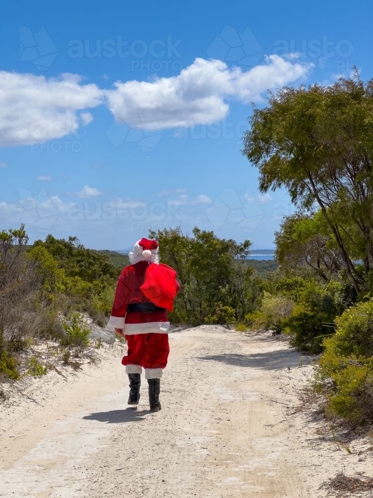Image of santa claus walking away down white sandy road with his sack ...