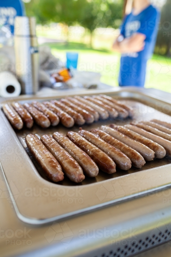 Sausages in a row cooking on park bbq warm lunch food for winter - Australian Stock Image