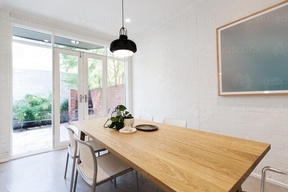 Scandi styled dining room interior with outlook to courtyard through french doors - Australian Stock Image