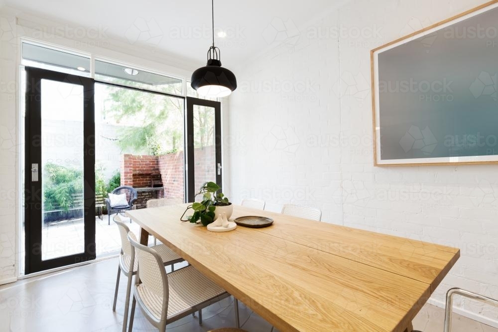 Scandi styled dining room interior with outlook to courtyard through open french doors - Australian Stock Image