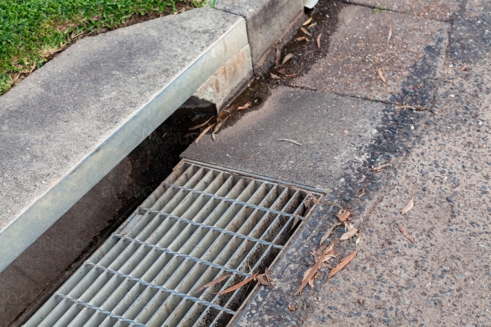 Scattering of leaves and water draining down drain in side of road - Australian Stock Image