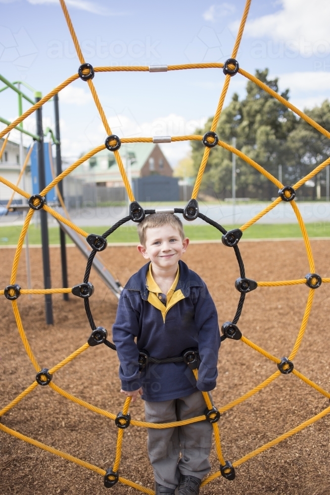 School age boy in centre of climbing net at playground - Australian Stock Image