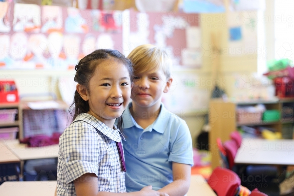 School boy and girl sitting on desk in classroom - Australian Stock Image