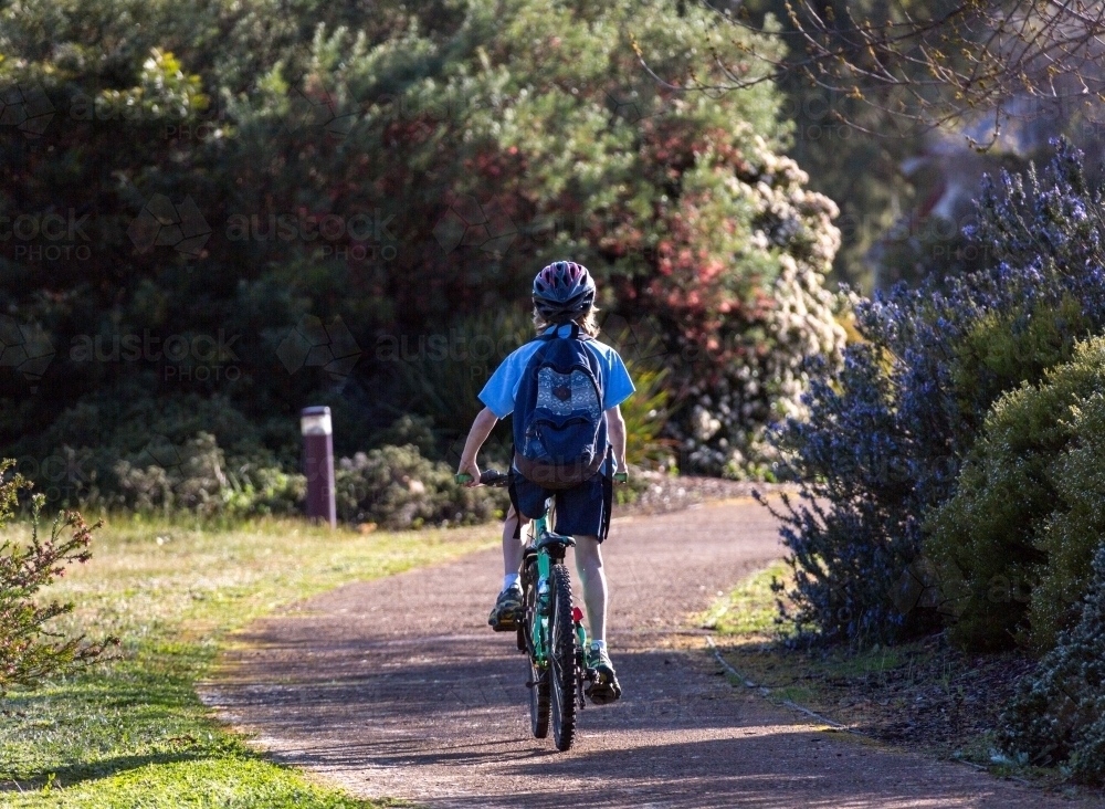 School child with backpack riding bicycle - Australian Stock Image