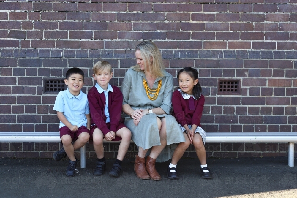 School children and their teacher sitting on a school bench outside - Australian Stock Image