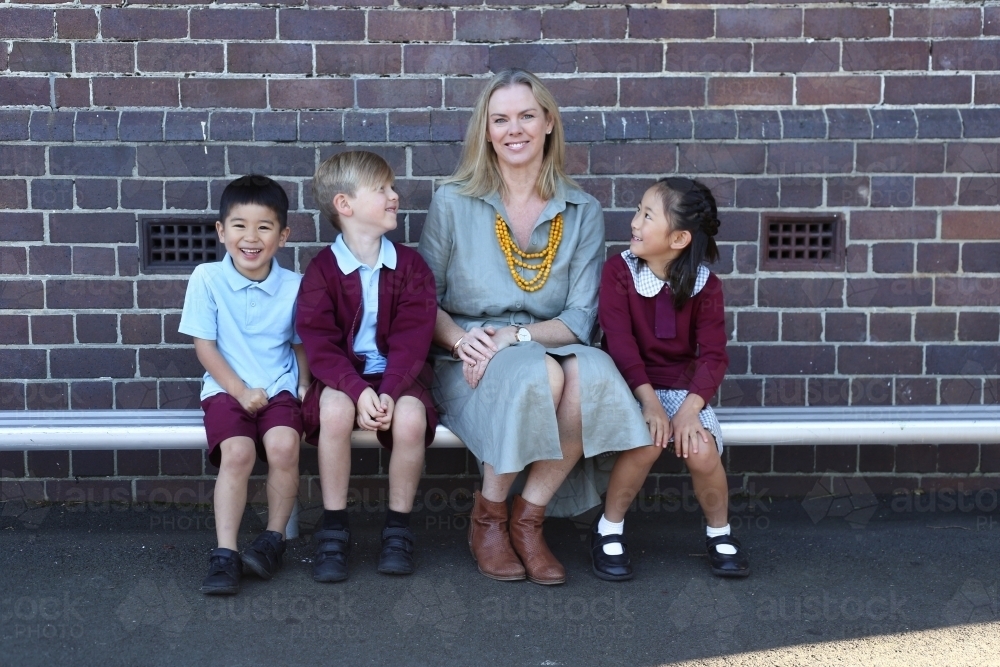 School children sitting and talking with their teacher in the school playground - Australian Stock Image