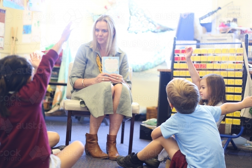 School children sitting on floor with hands up, ready to answer teacher's question - Australian Stock Image