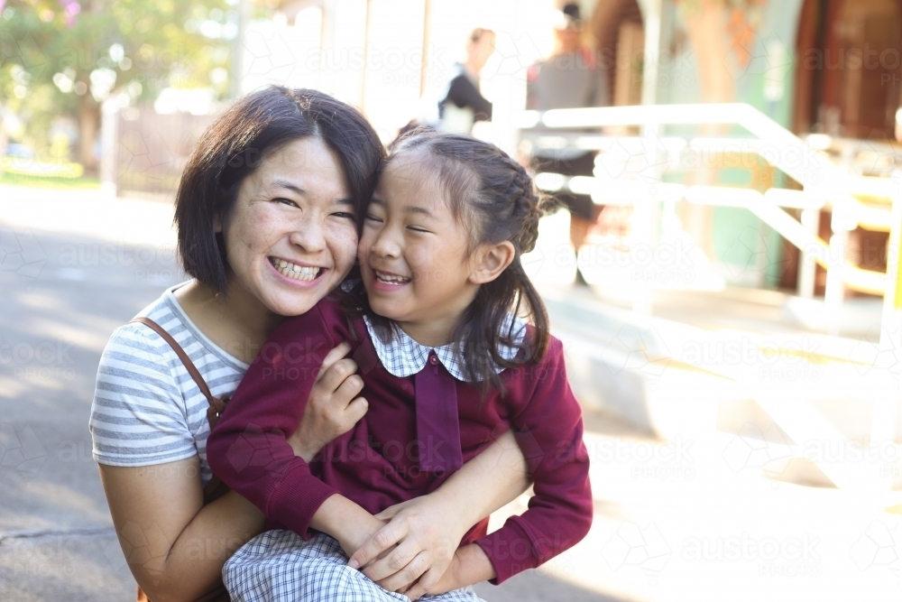 School girl sitting on her mother's knee, smiling and laughing - Australian Stock Image