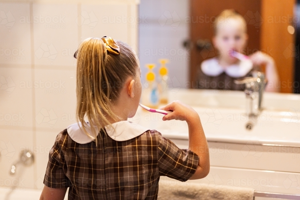 School kid in bathroom brushing her teeth in front of the mirror - Australian Stock Image