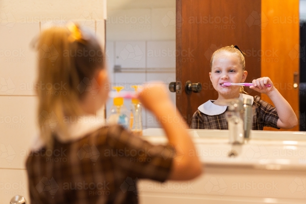 School kid in bathroom brushing her teeth in front of the mirror - Australian Stock Image