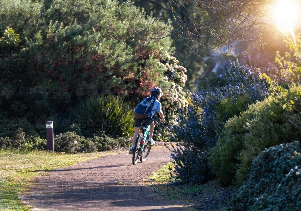 School kid riding to school through park gardens - Australian Stock Image