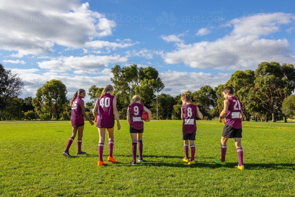 school kids walking onto football oval with afl balls seen from behind - Australian Stock Image