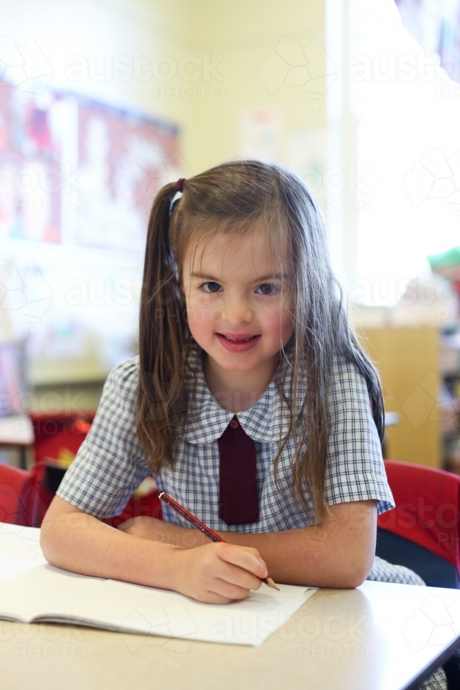 School student sitting at school desk smiling at camera - Australian Stock Image