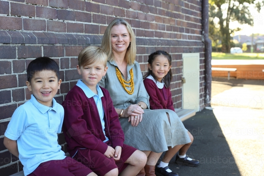 School students sitting with their teacher in the playground - Australian Stock Image