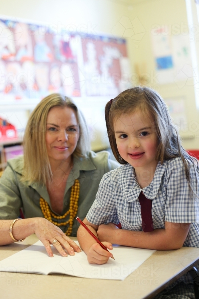 Image of School teacher helping child with her writing work - Austockphoto