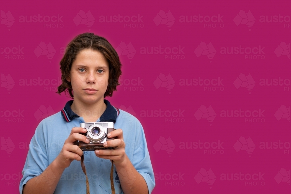 schoolboy holding vintage camera in front of magenta background - Australian Stock Image