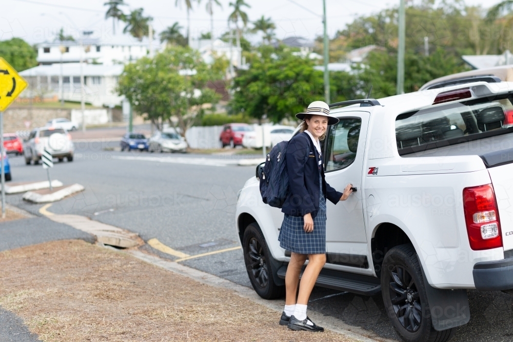 Schoolgirl in uniform about to open car door in street - Australian Stock Image