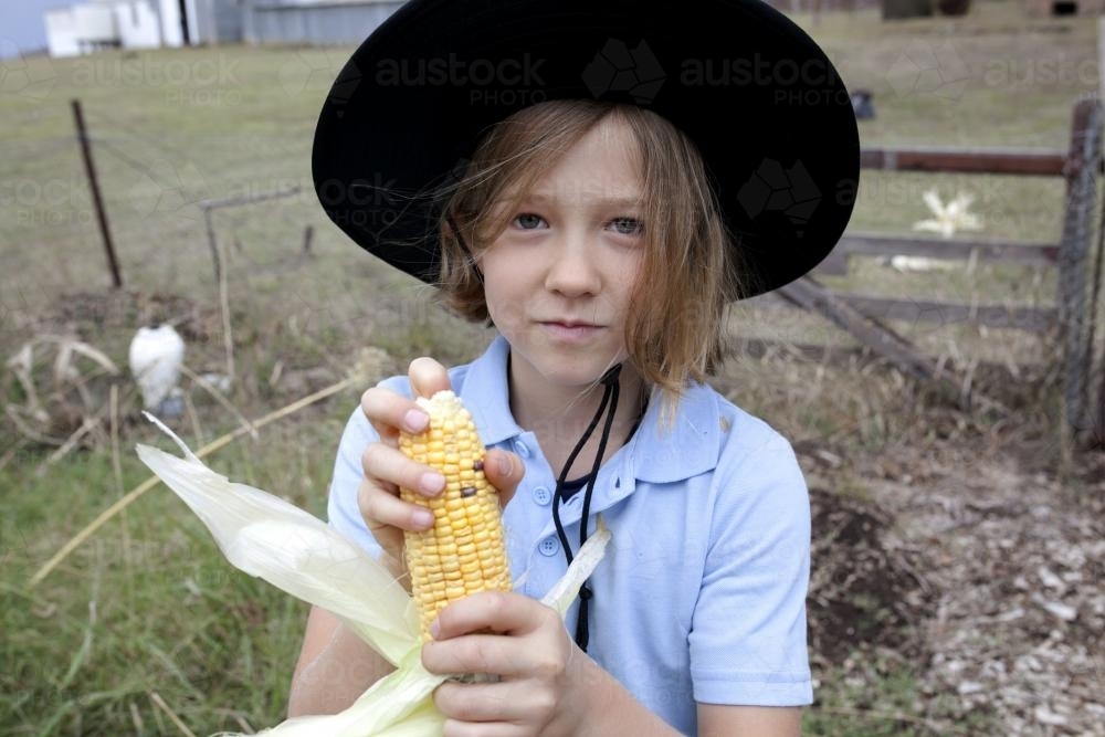 Schoolgirl wearing uniform and hat holding freshly picked corn - Australian Stock Image