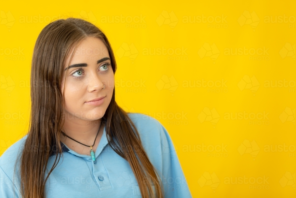 schoolgirl with long hair looking upwards on yellow background - Australian Stock Image