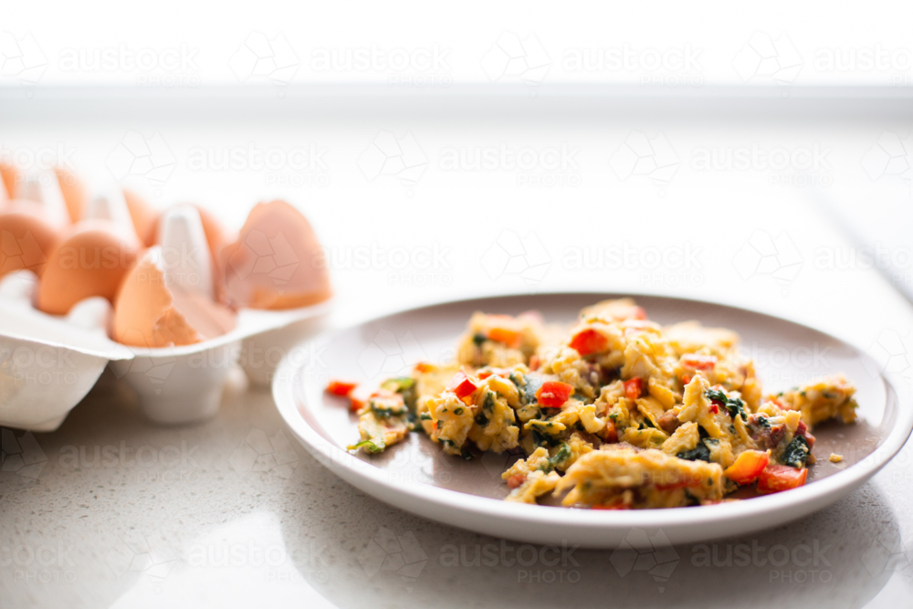 Image of scrambled eggs with veggies on a plate in a kitchen - Austockphoto