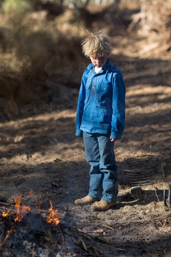 Scruffy kid standing near campfire - Australian Stock Image