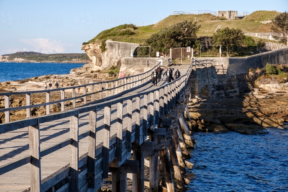 Scuba divers walking across bridge to Bare Island - Australian Stock Image