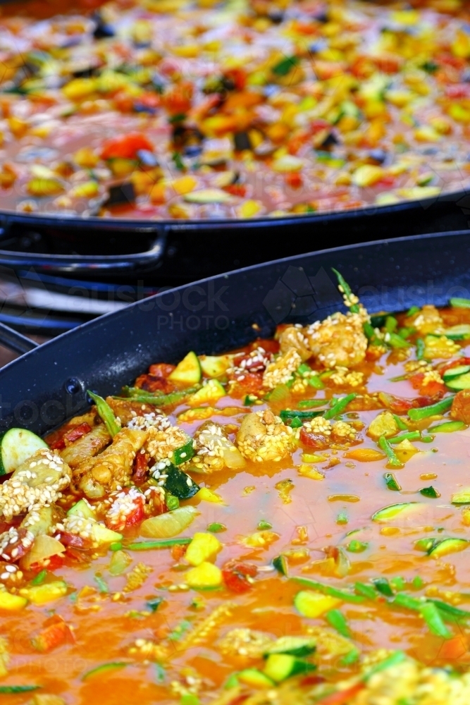 Seafood paella and lots of vegetables being cooked at a street market in very large pans. - Australian Stock Image