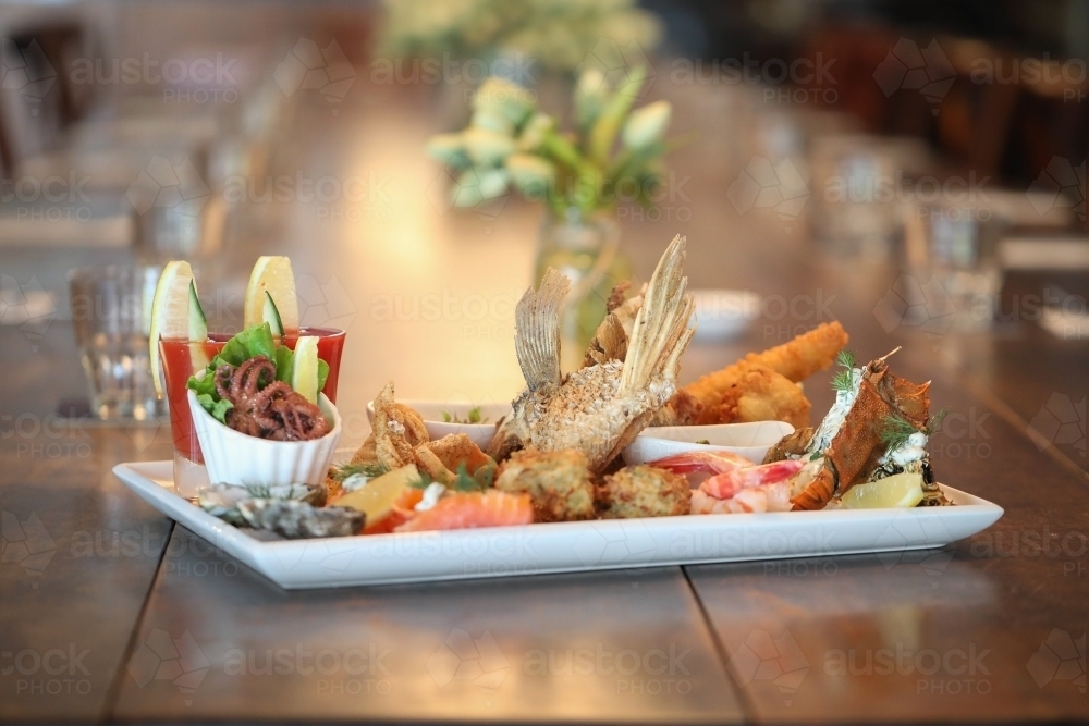 Seafood platter in restaurant setting featuring squid, prawns and barramundi wings - Australian Stock Image