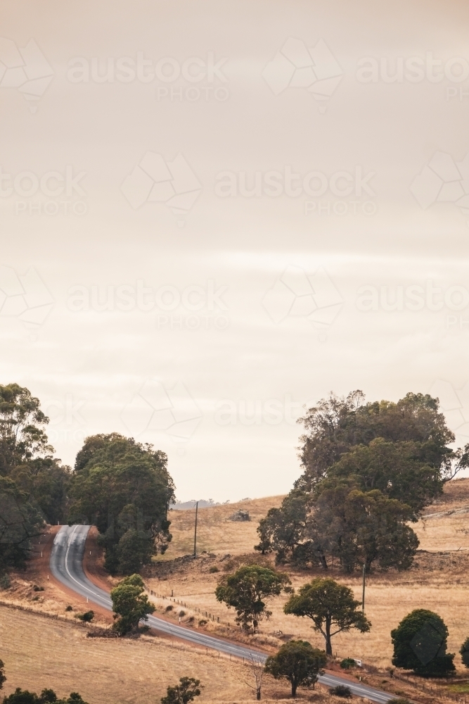 Sealed rural road winding uphill through farm land - Australian Stock Image
