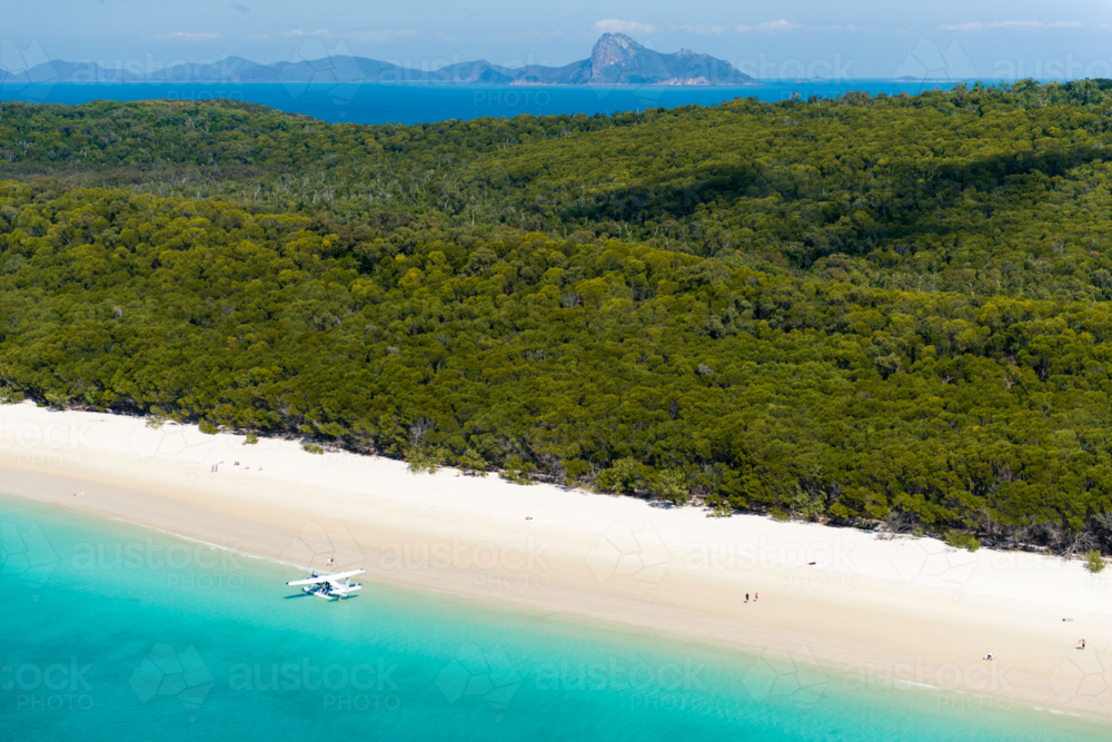 Seaplane moored on a remote tropical beach below dense coastal forest - Australian Stock Image