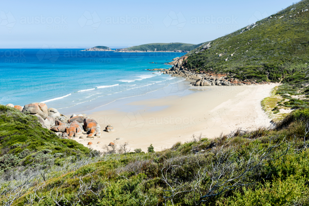 Secluded beach with orange-tinted boulders and clear blue water - Australian Stock Image