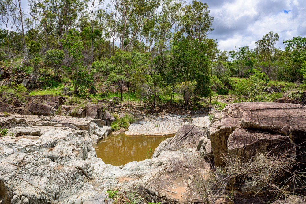 Secluded natural waterhole among rugged exposed rock formations and eucalyptus bushland - Australian Stock Image