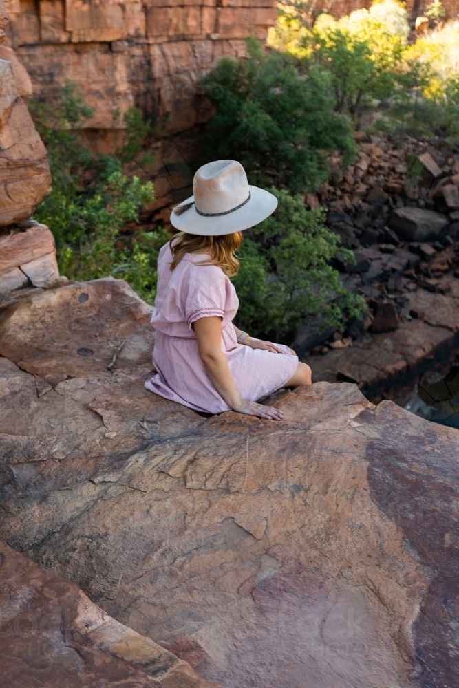 seen from behind young woman sitting on rock ledge in East Kimberley - Australian Stock Image
