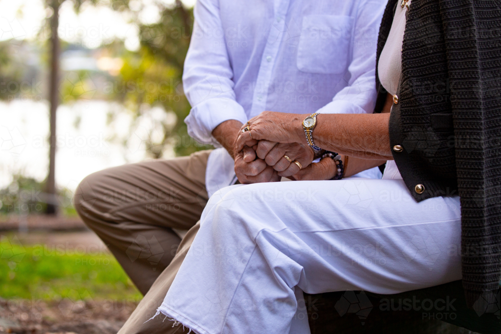 Image of Senior couple sitting on park bench holding hands. - Austockphoto
